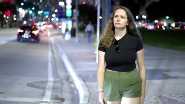 Mladá žena ztracená v myšlenkách kráčí po ulici v noci — Stock video