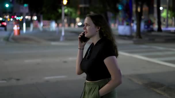 Mujer joven camina por la calle por la noche mientras recibe una llamada telefónica — Vídeos de Stock
