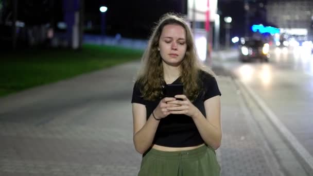 Geceleri sokakta yürürken cep telefonuyla mesajlaşan genç bir kadın. — Stok video