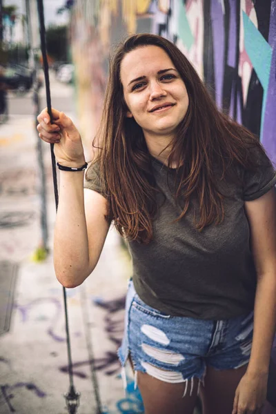 Mulher jovem e bonita se inclina contra uma parede colorida e posa para a câmera - estilo típico de rua — Fotografia de Stock