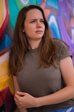 Genç ve güzel bir kadın renkli bir duvara yaslanır ve kameraya poz verir - tipik sokak tarzı.