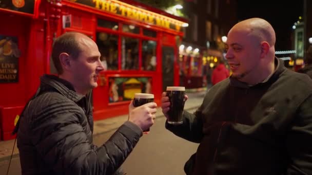 Dos amigos tomando una cerveza en el barrio Temple Bar de Dublín de noche - fotografía de viaje — Vídeo de stock