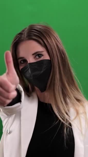 戴口罩的年轻女子竖起大拇指做手势 工作室摄影 垂直录像 — 图库视频影像
