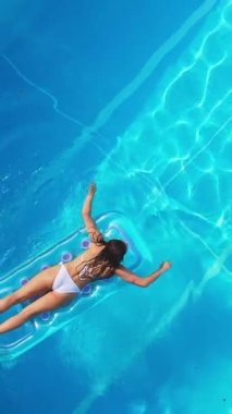 Pretty girl lies on an air mattress in the swimming pool - view from above - Vertical video