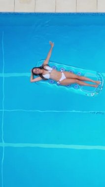 Sexy girl enjoys the sun in the crystal clear water of a swimming pool - view from above - Vertical video