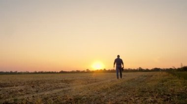 Çiftçi gün batımında yürüyor. Çiftçilik. Çiftçi silueti. Elinde dijital tabletle, gün batımında ya da yükselen güneşin altında biçilmiş bir tarlada yürüyen çiftçi. tarım tarım sektörü kavramı.
