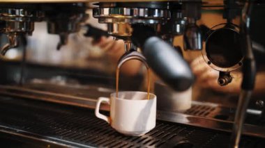 Kahve içeceğim. Yakın plan. Kahveci kahve makinesini kullanarak kahve hazırlar. İnce kahve akıntısı espresso makinesinden küçük beyaz bir fincana akar..