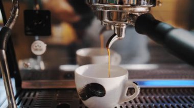 Kahve içeceğim. Yakın plan. Kahveci kahve makinesini kullanarak kahve hazırlar. İnce kahve akıntısı espresso makinesinden küçük beyaz bir fincana akar..