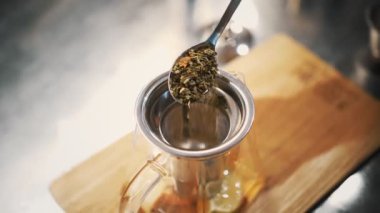 Çay içeceğim. Çay hazırlıyorum. Yakın plan. Üst Manzara. Bir kaşık dolusu kuru, çiçek, çaydanlığa yapraklı yeşil çay dökülüyor. Meyveli sıcak içecek.