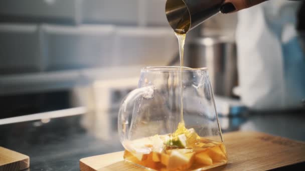 Bebida de té. haciendo té. preparación de bebidas. Primer plano. maestro del té vierte jarabe dulce o jugo en una tetera de vidrio con trozos de fruta para una mayor preparación de la bebida especial de té de frutas calientes — Vídeos de Stock