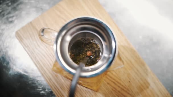 เครื่องดื่มชา เตรียมชา ท็อปวิว ใกล้ชิด น้ําเดือดเทลงในกาน้ําชาแก้วพร้อมชาเขียวใบ เครื่องดื่มร้อนผลไม้เบอร์รี่ ชาไอน้ํา — วีดีโอสต็อก