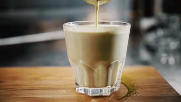 Cappuccino matcha. primo piano. barista è filtrante mix bevanda di latte e tè verde matcha attraverso un setaccio. il cocktail è versato a un bicchiere. — Video Stock
