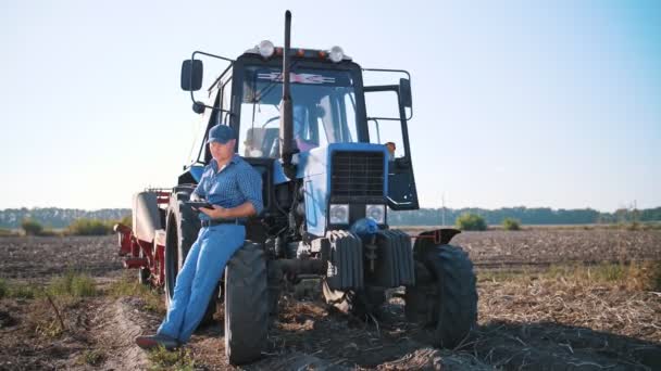 CHERKASSY, UKRAINE, SEPTEMBER 24, 2021: збирання картоплі. Фермер користується цифровим планшетом. на фермі, на фермі, на задньому плані. трактор з картопляним жниварником. розумне господарство. сільськогосподарські технології — стокове відео