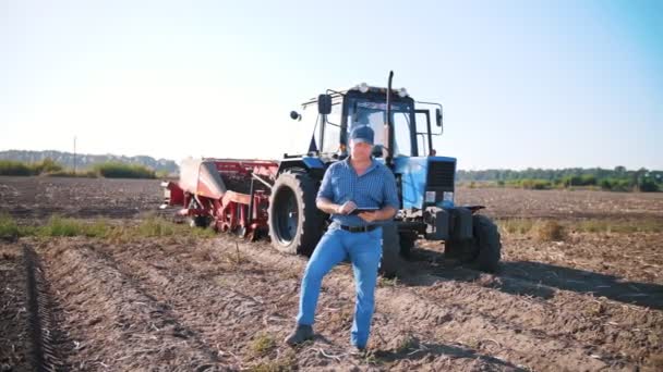 Уборка картофеля. фермер с помощью цифрового планшета. на фермерском поле, на фоне сельскохозяйственной техники. трактор с картофельным комбайном. умное фермерство. сельскохозяйственные технологии — стоковое видео