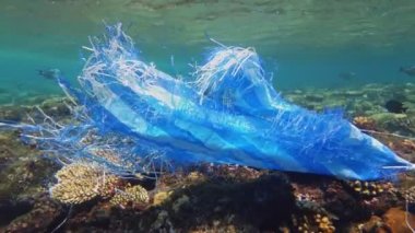 Denizde çöp. Denizin plastik kirliliği. Mavi plastik poşet güneş ışığında yavaşça suyun altında sürükleniyordu. Arka ışıklandırma. Plastik atık çevresel kirlilik sorunu