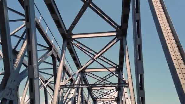 Pont métallique. constructions en fer brut contre le ciel bleu, filmé en mouvement à partir d'une voiture. vue du bas. Pont ferroviaire et routier traversant la rivière. Silhouette de traversée de poutres en acier. — Video