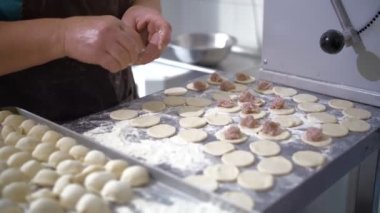Yarı bitmiş ürünler. Yemek pişirmek. Yakın plan. Aşçılar hamur, mantı, ravioli ve pelmeni yapmak için hamur parçalarının üzerine kıyma koyuyorlar. Açık büfe restoran mutfağı..