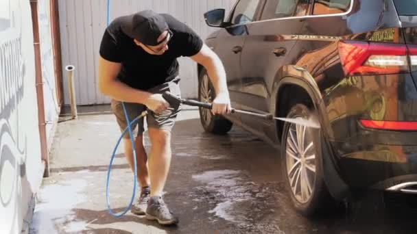 Um homem lava um carro com água limpa spray de alta pressão, fora, em auto-serviço de lavagem de carro. Limpeza de carro. — Vídeo de Stock