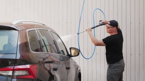 Un uomo lava un'auto con acqua pulita spray ad alta pressione, all'esterno, presso l'autolavaggio self-service. Pulizia auto. — Video Stock