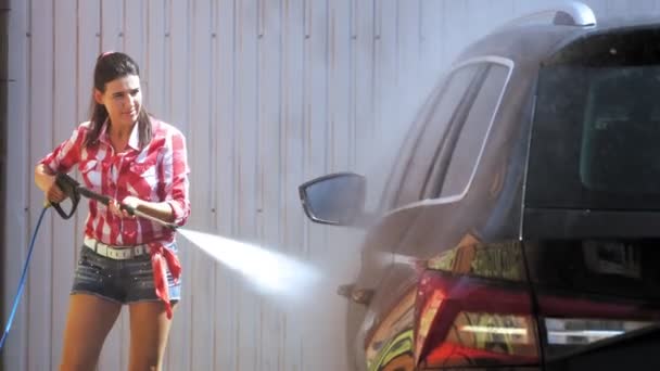 Güzel bir kadın, dışarıda oto yıkamada temiz su, yüksek basınçlı spreyle araba yıkar. Araba Temizleme. — Stok video