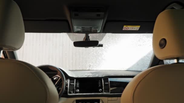 Myjnia samochodowa. Mężczyzna myje przednią szybę samochodu piankowym sprayem wysokociśnieniowym, w myjni samoobsługowej, na zewnątrz. Sprzątanie samochodu. Widok z wnętrza samochodu — Wideo stockowe