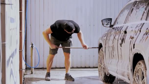 洗车。一个穿着黑色T恤的男人正在户外洗车，车上覆盖着肥皂泡，用一把特殊的刷子，在自助洗车。洗车 — 图库视频影像