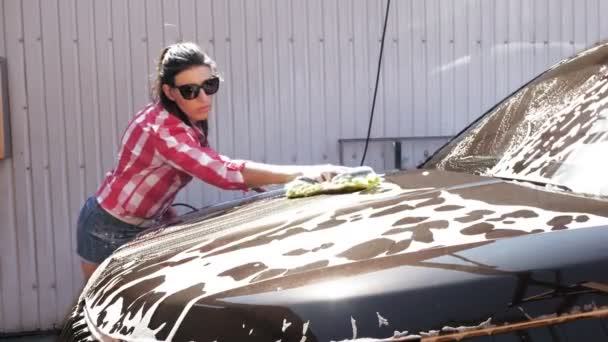 Autowäsche. Eine junge Frau in kurzen Hosen und Hemd wäscht ein mit Seifenschaum überzogenes Auto mit einem Waschlappen in einer Selbstbedienungswaschanlage im Freien. Autoreinigung — Stockvideo