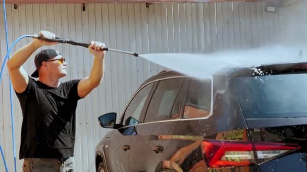 Автомийка. Чоловік миє автомобіль з розпилювачем високого тиску з чистою водою, при самообслуговуванні автомийкою, на відкритому повітрі. Прибирання автомобілів . — стокове відео