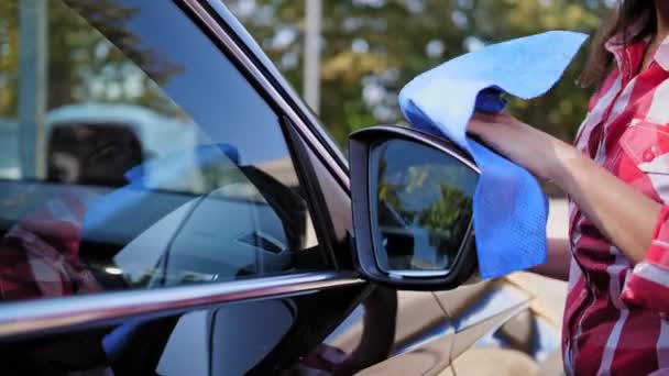Biltvätt, biltorkning. närbild. kvinnan torkar en bil, bakifrån visa glas med en trasa, utanför, efter tvätt, vid en självbetjäning biltvätt. Bilrengöring. — Stockvideo