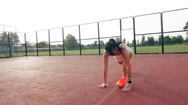 Fitness al aire libre. Mujer deportiva, en la parte superior blanca y pantalones cortos, zapatillas de deporte naranja y gafas de sol, está haciendo varios ejercicios en la cancha naranja con marcas blancas, en el estadio. Día de verano. Deportes al aire libre — Vídeo de stock