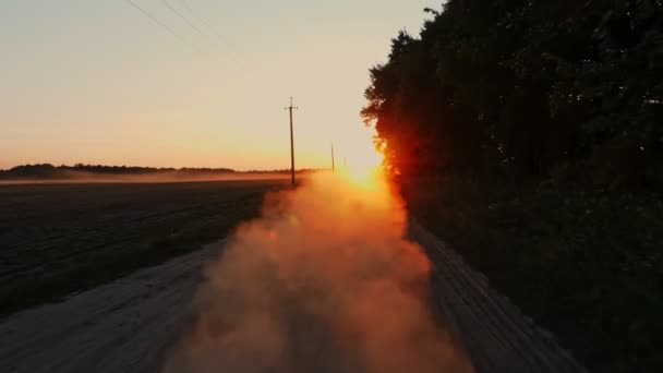 Strada polverosa. tramonto sul campo della fattoria. polveroso, strada sterrata lungo un campo agricolo e bosco, al tramonto. la polvere sale nell'aria. nubi di polvere salire — Video Stock