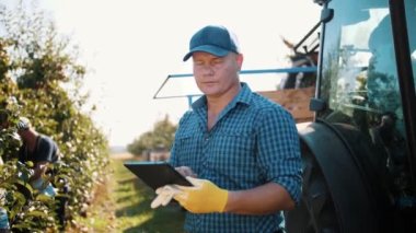 Elma hasadı. Tabletli çiftçi. Hasat teftişi. Tarım uzmanı dijital tablet kullanıyor, işçiler meyve bahçesinden elma topluyor. Bahçıvanlıkta, çiftçilikte modern teknoloji. Tarım teknolojisi.