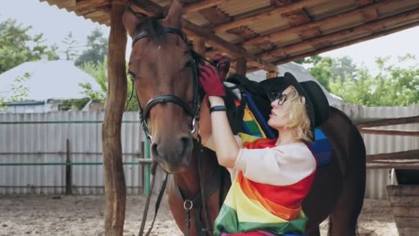 Regnbågsflagga. hästvård. Hästsport hobby. en ryttare flicka, med lgbt regnbåge symboler, sätter på betsel, tyglar på sin häst. Bisexuell, transsexuell eller lesbisk kvinna. — Stockvideo