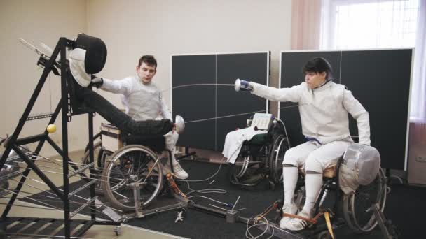 Atleta com deficiência. Esgrima. treino de atletas de esgrima de cadeira de rodas com habilidades físicas reduzidas. Eles praticam a técnica de duelo de luta em um simulador especial. — Vídeo de Stock
