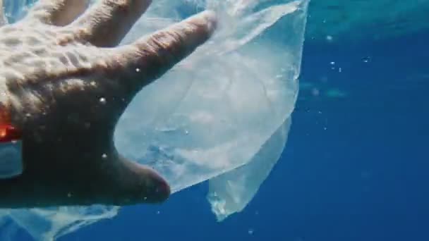 Σκουπίδια στη θάλασσα. Καθαρίστε τη θάλασσα. συλλέγουν σκουπίδια στο νερό. Κοντινό πλάνο. Το αρσενικό χέρι αρπάζει απόβλητα, χρησιμοποιημένες πλαστικές σακούλες. άποψη πρώτου προσώπου. ρύπανση της θάλασσας ή των ωκεανών. προστασία του περιβάλλοντος. — Αρχείο Βίντεο