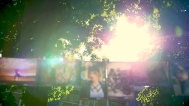 Sokak dekorasyonu. İple çekilmiş fotoğraflar. Üzerinde fotoğraflar olan çelenk. Fotoğraflar asılı, mandallarla bağlanmış, ipe asılmış. Yaz güneşinin arka planında yeşil yapraklar.