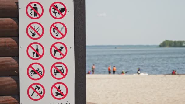 Verbotsplakat. Verbotsschild. Nahaufnahme. Plakat mit Verbotsschildern am Strand. vor der Kulisse von Meer, Sandstrand und Urlaubern. verschwommener Hintergrund. — Stockvideo