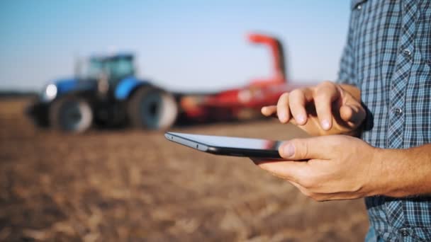 デジタルタブレットを使う農家です。接近中だ。農業機械を背景にしています。ジャガイモ収穫機付きトラクター。賢い農業だ。農業技術です。ジャガイモの収穫. — ストック動画