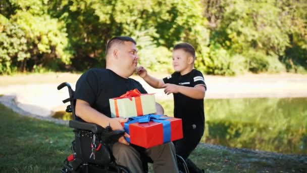 Ημέρα πατέρων. Το χαριτωμένο αγοράκι δίνει δώρα στον μπαμπά του. Ένας άντρας είναι άτομο με αναπηρία. Χρήστης αναπηρικής πολυθρόνας άτομα με ειδικές ανάγκες. — Αρχείο Βίντεο