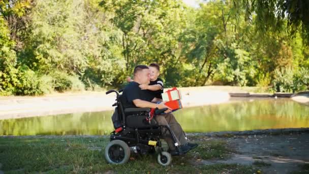 Fathers day. little cute boy gives gifts to his dad. a man is a person with disability. wheelchair user. people with special needs. — Stock Video