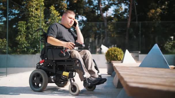 Person med funktionshinder. rullstolsburen. personer med särskilda behov. Unge man pratar i telefon, i parken, på sommardagen. Han använder rullstol. — Stockvideo