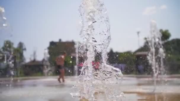 Fuente. Primer plano. chorros de fuente. sobre el fondo son niños borrosos, que se divierten entre los arroyos de agua, chorros de alta fuente en el parque de la ciudad, en el día de verano caliente. — Vídeo de stock