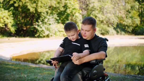 Apák napja. Apa és fia. Apa és a kisfia együtt töltik az időt, jól érzik magukat. fogyatékossággal élő személy. különleges igényű emberek. kerekesszék-használó. — Stock videók