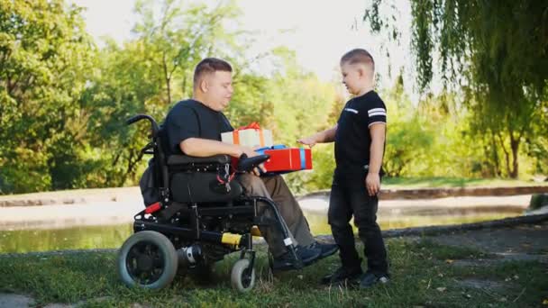 Fathers day. little cute boy gives gifts to his dad. a man is a person with disability. wheelchair user. people with special needs. — Stock Video