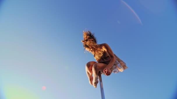 Полюсний танець. Підійде гімнастка в бежевому леопарді, виконує акробатичні вправи на металевому полюсі, що обертається навколо блакитного неба. вид знизу вгору — стокове відео