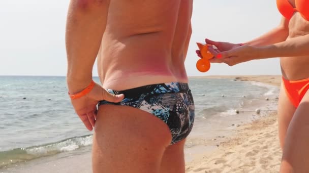 Αντηλιακό. ασφαλές μαύρισμα. ηλιακό έγκαυμα. προστασία από την επιβλαβή ηλιακή ακτινοβολία. Κοντινό πλάνο. γυναίκα εφαρμόζει αντηλιακό για τους άνδρες δέρμα του σώματος. Παραλία, θάλασσα. ηλιόλουστη ζεστή μέρα — Αρχείο Βίντεο