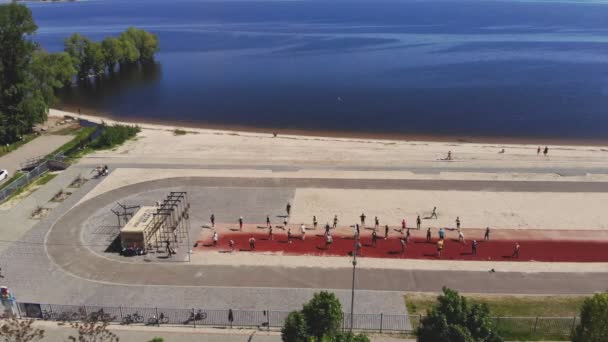 CHERKASSY, UKRAINE, 25 - го травня 2021 р.: групова підготовка на відкритому повітрі. Фітнес на вулиці. Повітряний вид. Велика група людей, одягнена в активацію, тренується разом, на пляжі, біля моря, на відкритому повітрі. — стокове відео