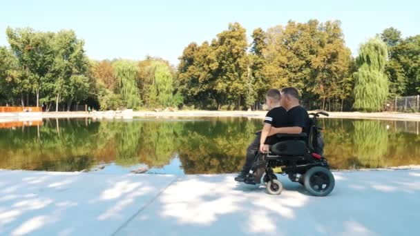 Día de los padres. persona con una discapacidad. Papá y su pequeño hijo lindo están caminando en el parque, en el día de verano. Papá es un usuario de silla de ruedas. personas con necesidades especiales. — Vídeos de Stock