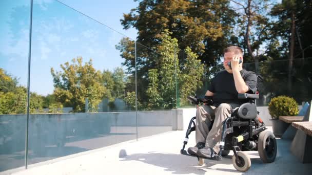 Osoba se zdravotním postižením. uživatele invalidního vozíku. lidé se zvláštními potřebami. Ten mladík mluví po telefonu, v parku, v letní den. Je to uživatel invalidního vozíku. — Stock video