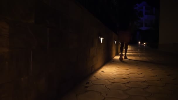 Plimbări de seară. Cale cu lumini noaptea. De aproape. picioare de sex feminin, în adidași, merge de-a lungul drumului. felinare de grădină, lumini sunt situate de-a lungul drumului — Videoclip de stoc